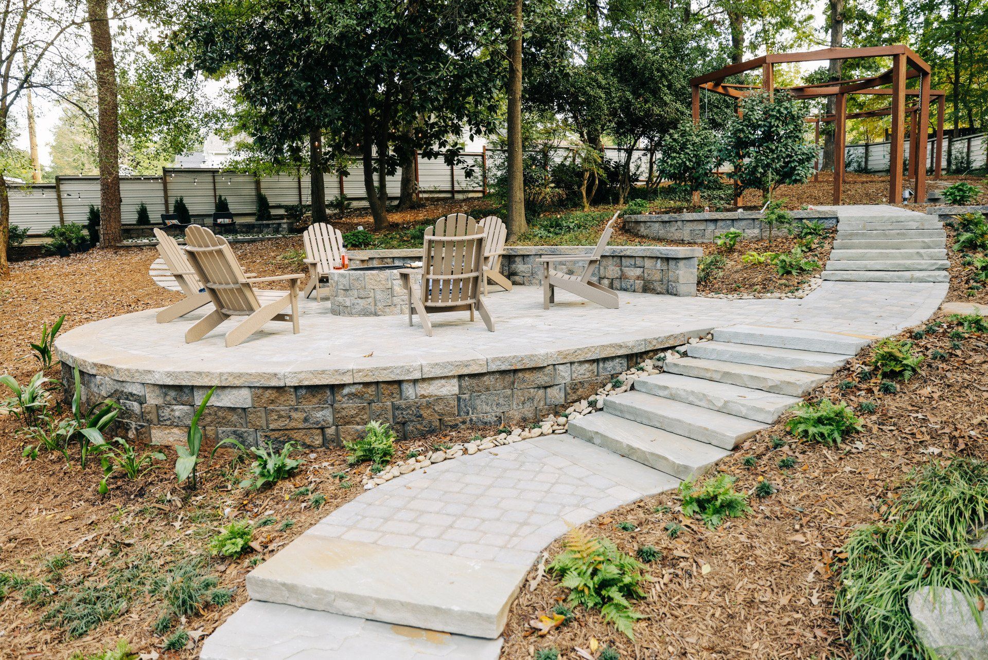 Outdoor stone patio with lounge chairs, fire pit, and steps leading to a raised pergola seating area.