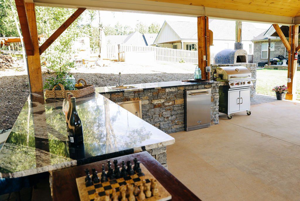 Covered outdoor patio with granite bar and built-in grill overlooking a backyard and pool