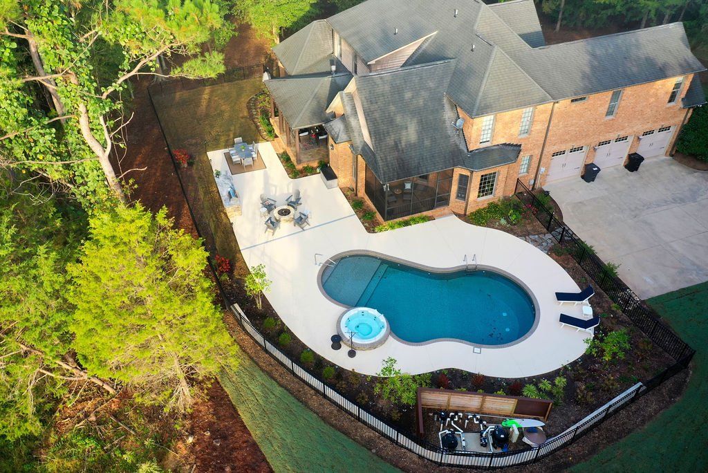 Aerial view of a house with a backyard pool, patio seating, and surrounding trees