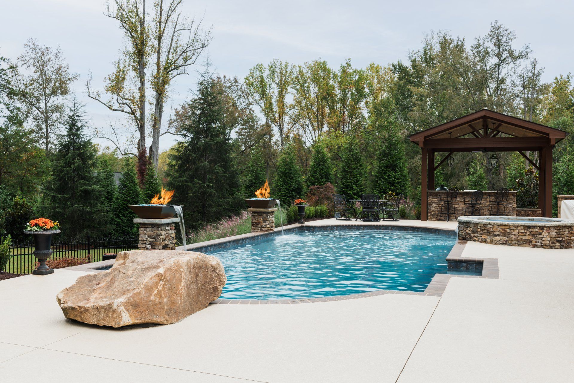 Backyard pool with stone accents, a large boulder, and a wooden gazebo surrounded by trees