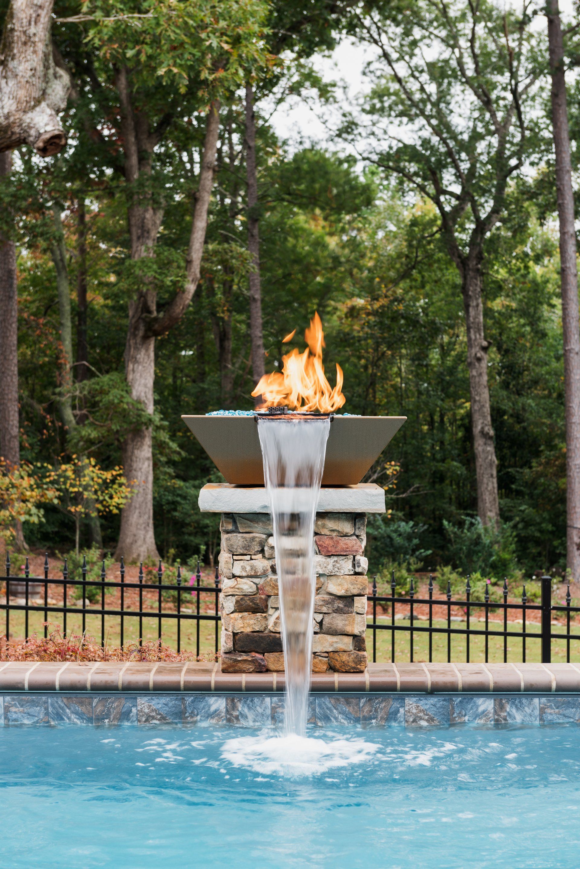 Poolside fountain with fire and flowing water in a wooded outdoor setting