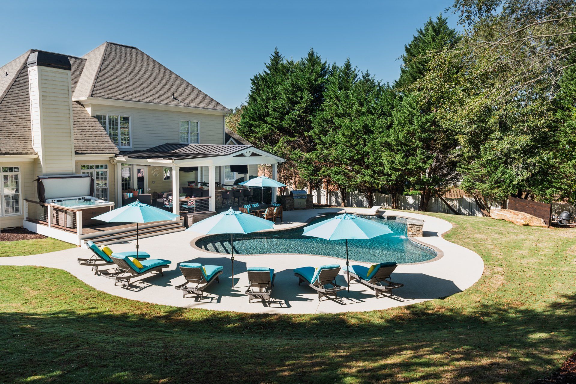 Backyard pool patio with lounge chairs, umbrellas, and a house in the background