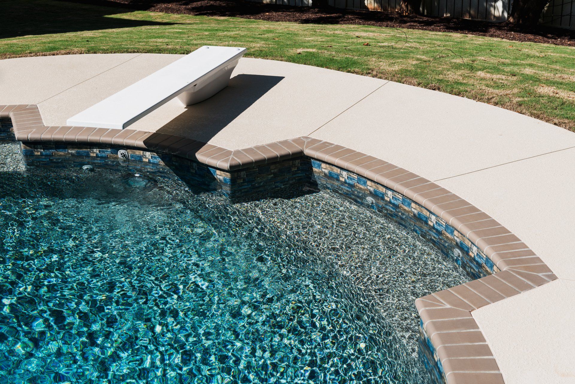 Curved swimming pool with blue water, tan deck, and a white diving board平台