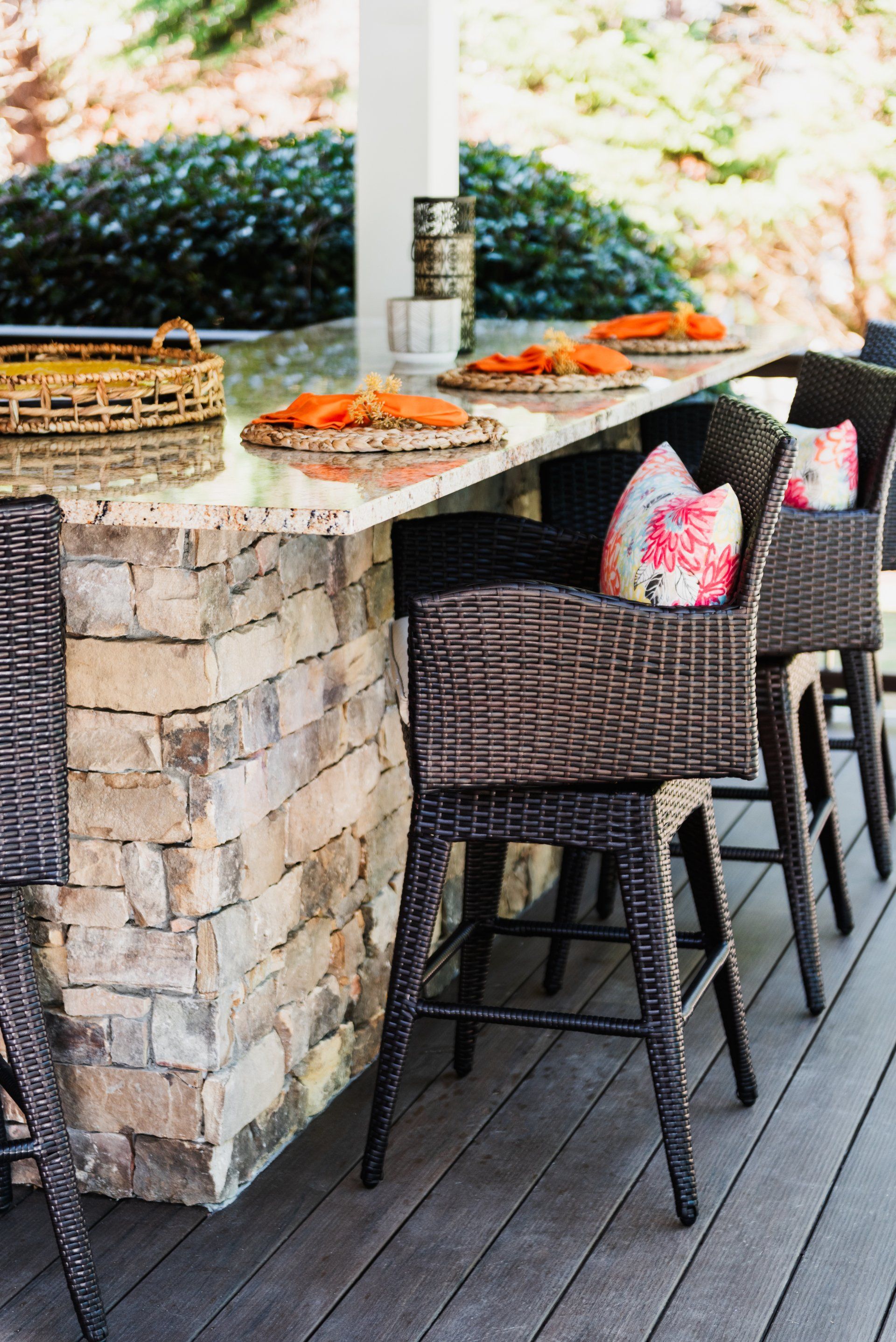 Outdoor patio bar with wicker stools, stone counter, and trays of food on a wooden deck