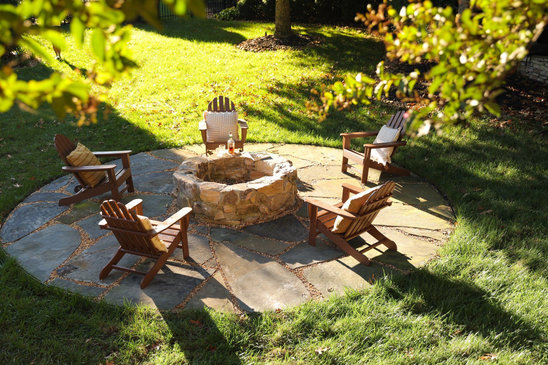 Outdoor stone fire pit with wooden chairs on a sunlit patio in a garden
