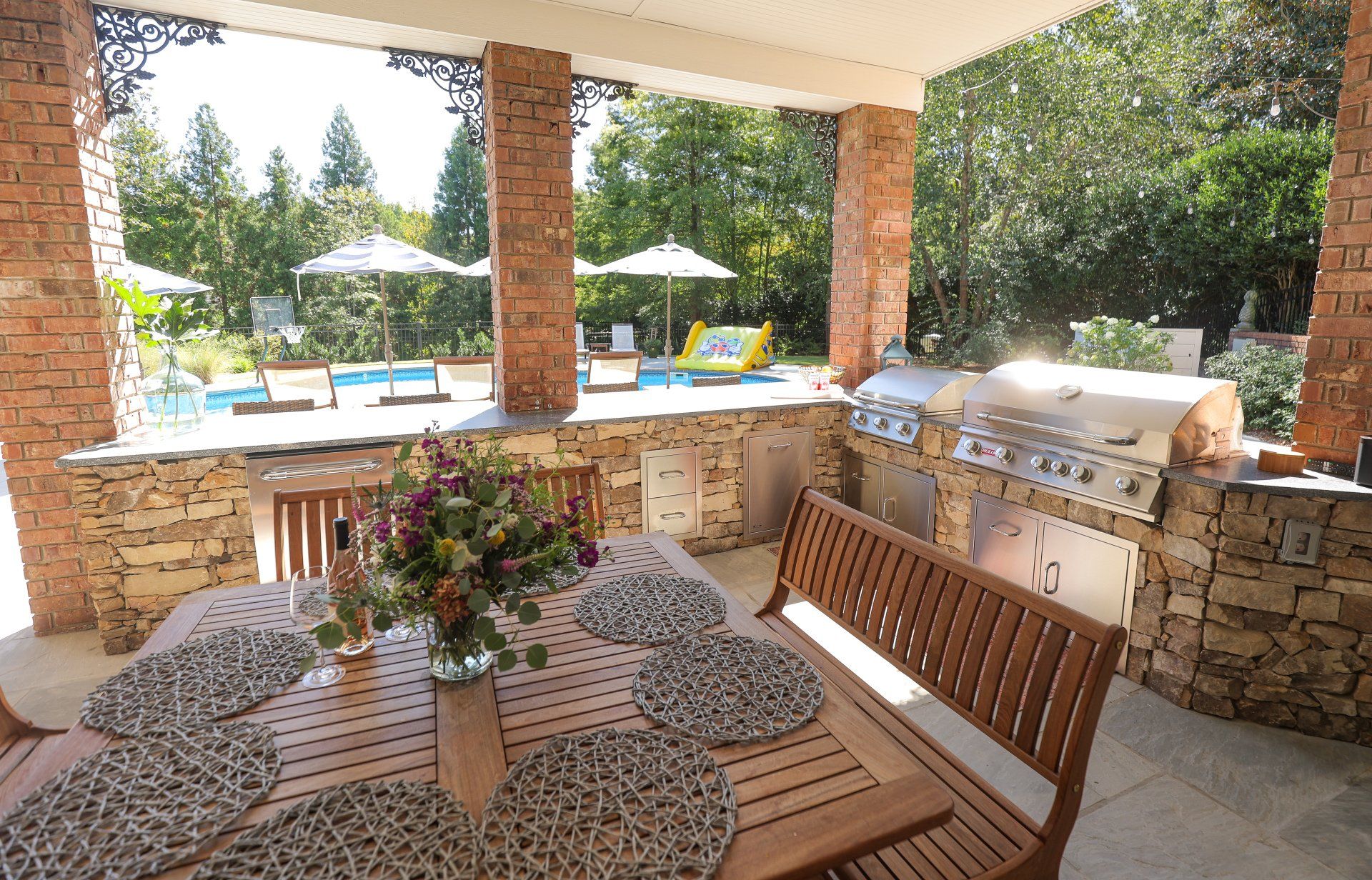 Covered patio with wooden bench and table overlooking a pool and lounge chairs.