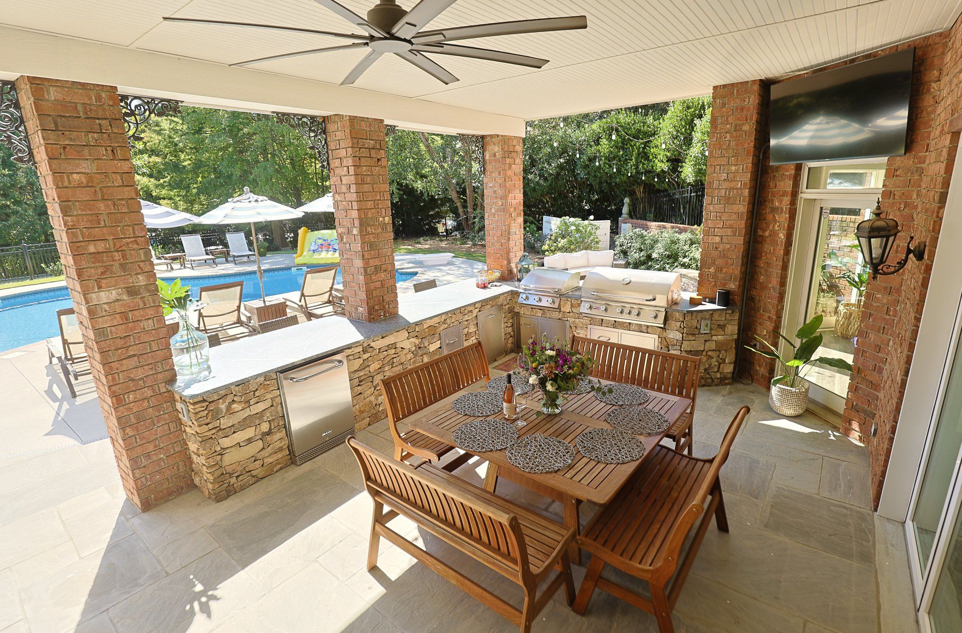 Covered patio with dining table, wooden chairs, and a pool view through brick columns