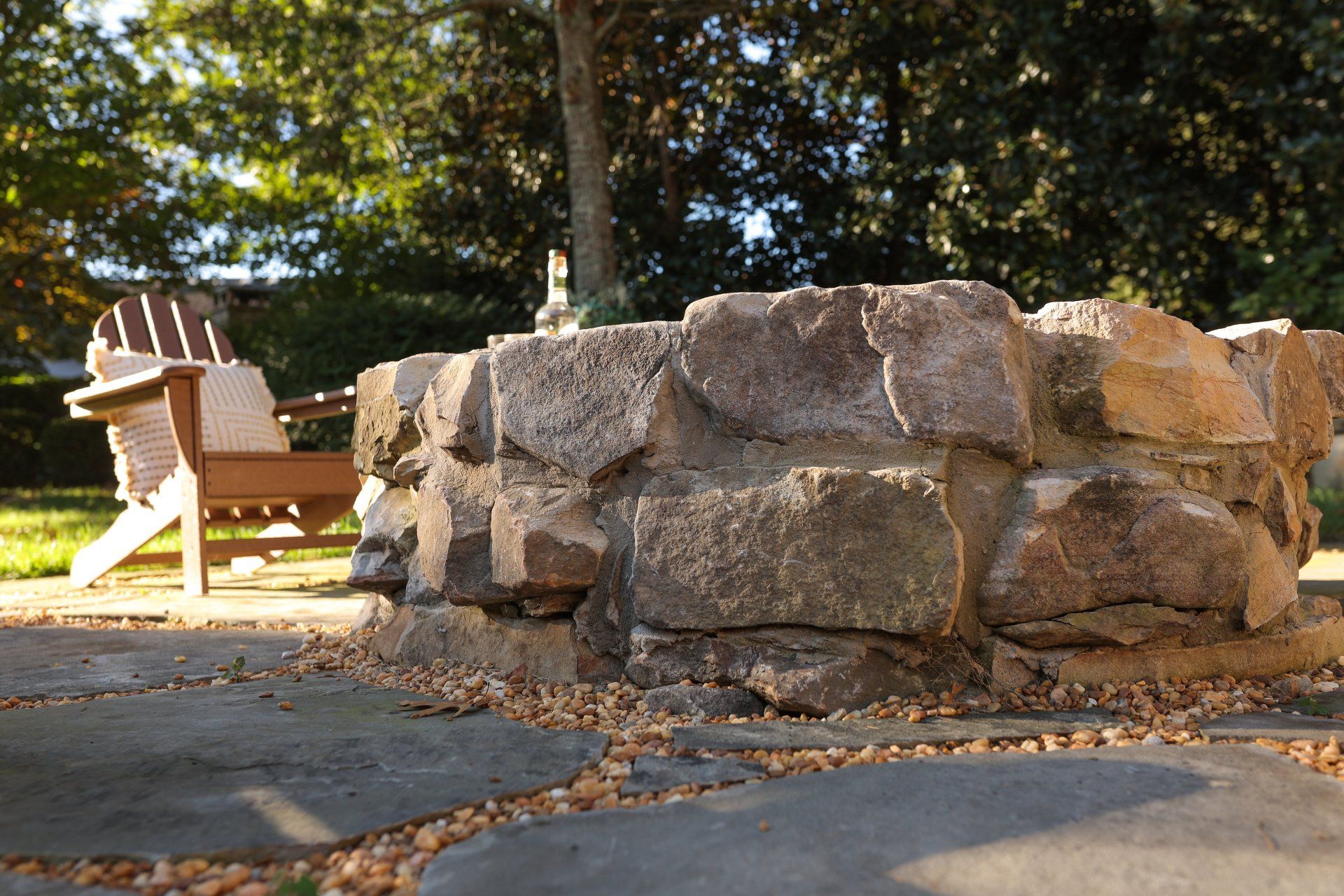 Stone fire pit in a park with a wooden bench and trees in the background