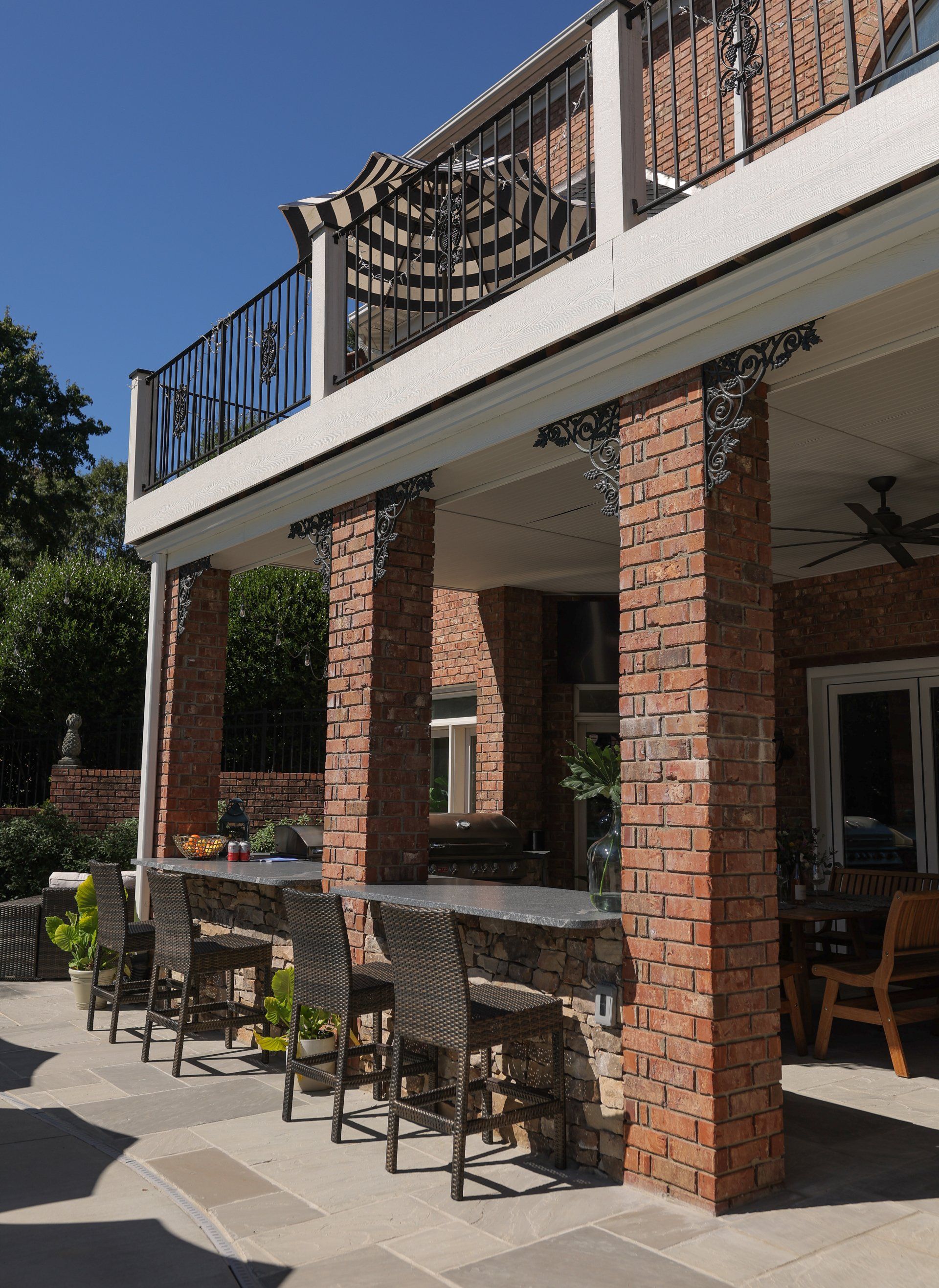 Brick patio and covered balcony with black railing, tables, and chairs beside a house