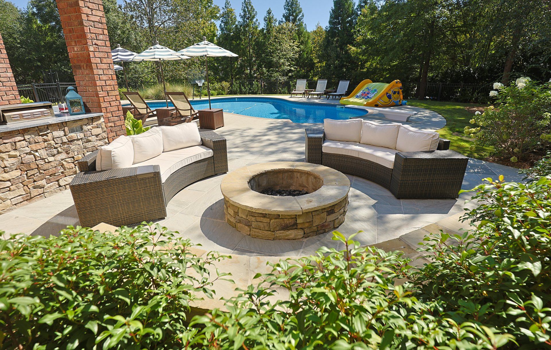 Backyard patio with curved seating around a fire pit beside a swimming pool and lush greenery