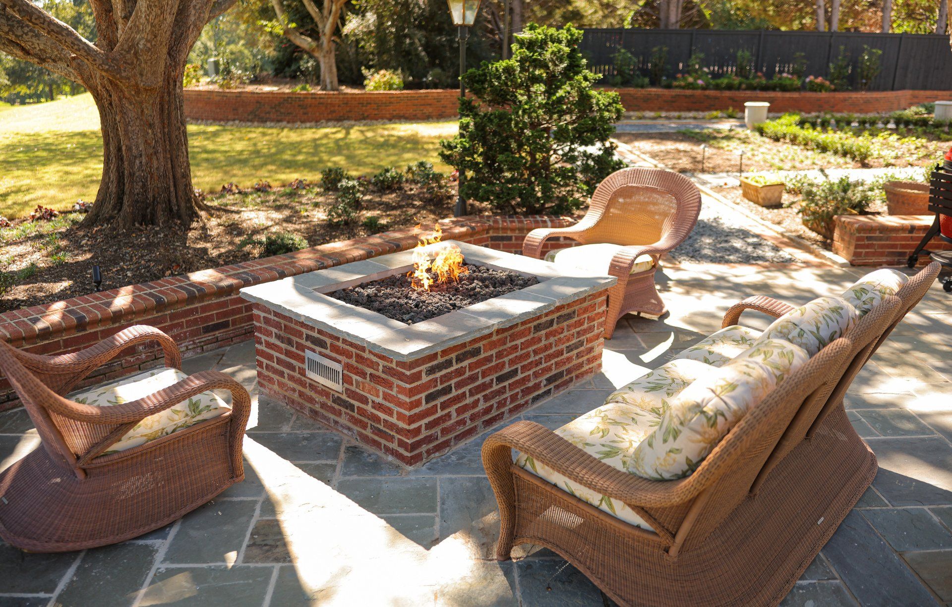Outdoor brick fire pit surrounded by wicker chairs on a bluestone patio in a garden