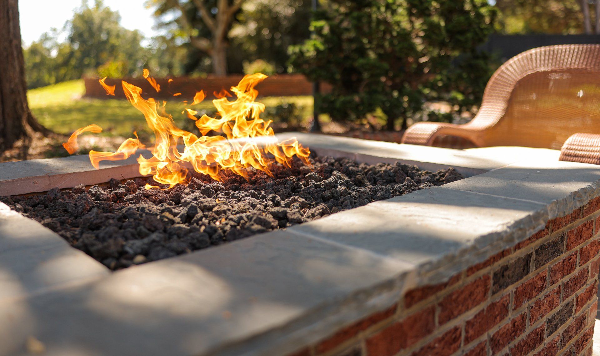 Outdoor brick fire pit with active flames and patio seating nearby