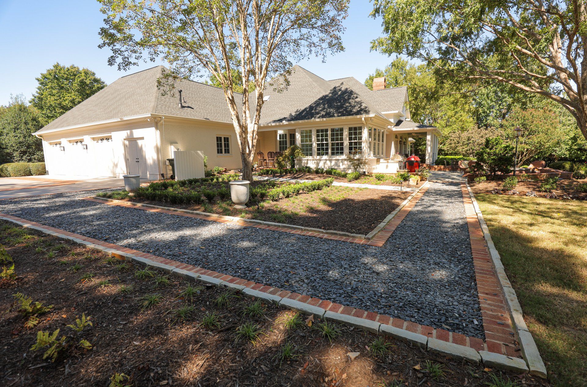 Brick house with a gravel courtyard, brick edging, and trees in a sunny landscaped yard