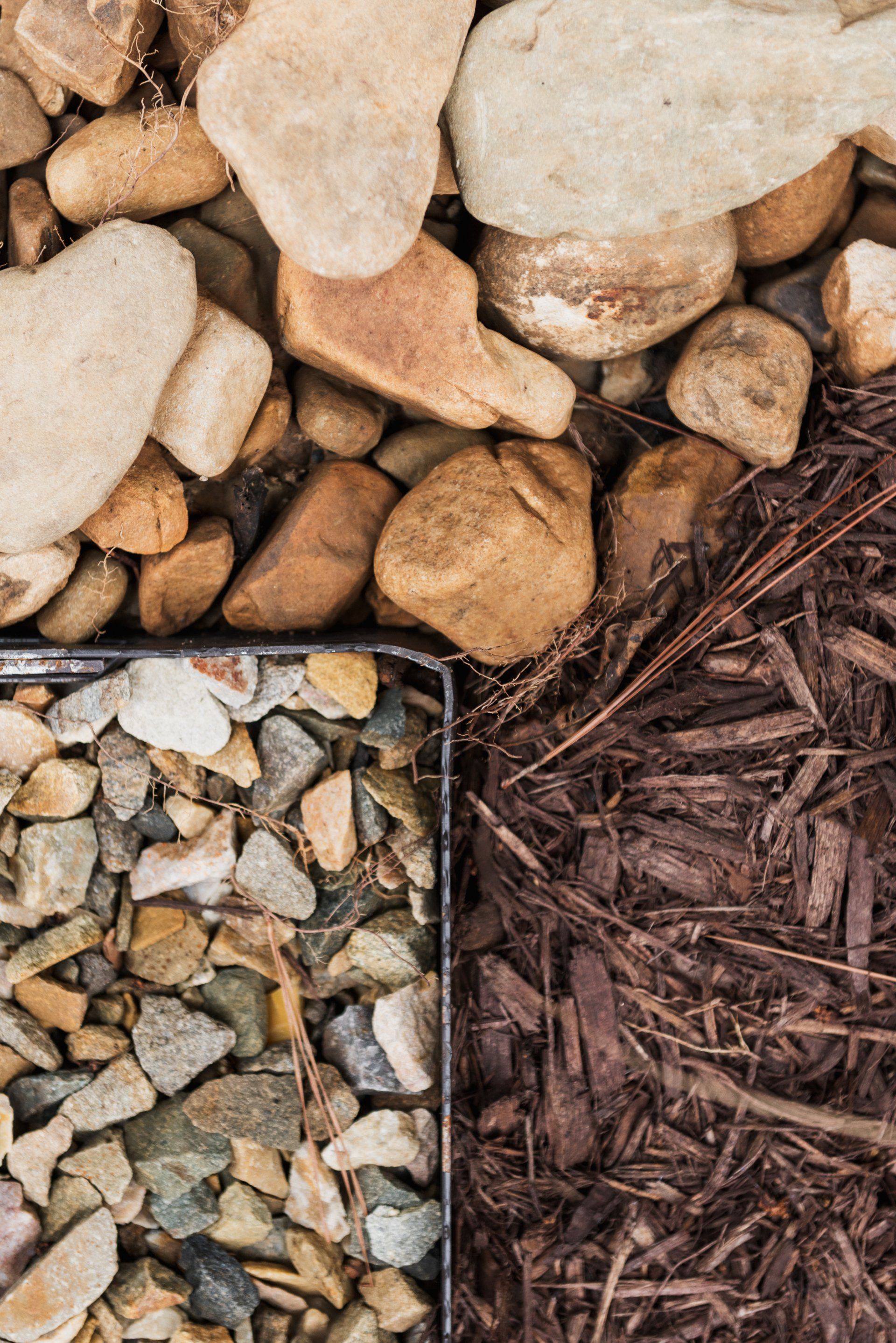 Close-up of decorative ground cover with tan stones, gray gravel, and brown mulch in sections