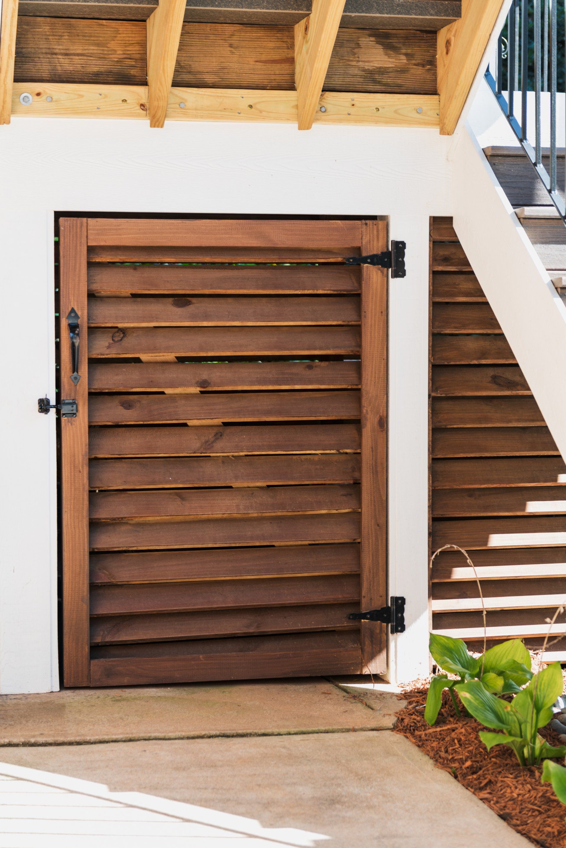Wooden slatted door beneath an overhang beside stairs and a potted plant.