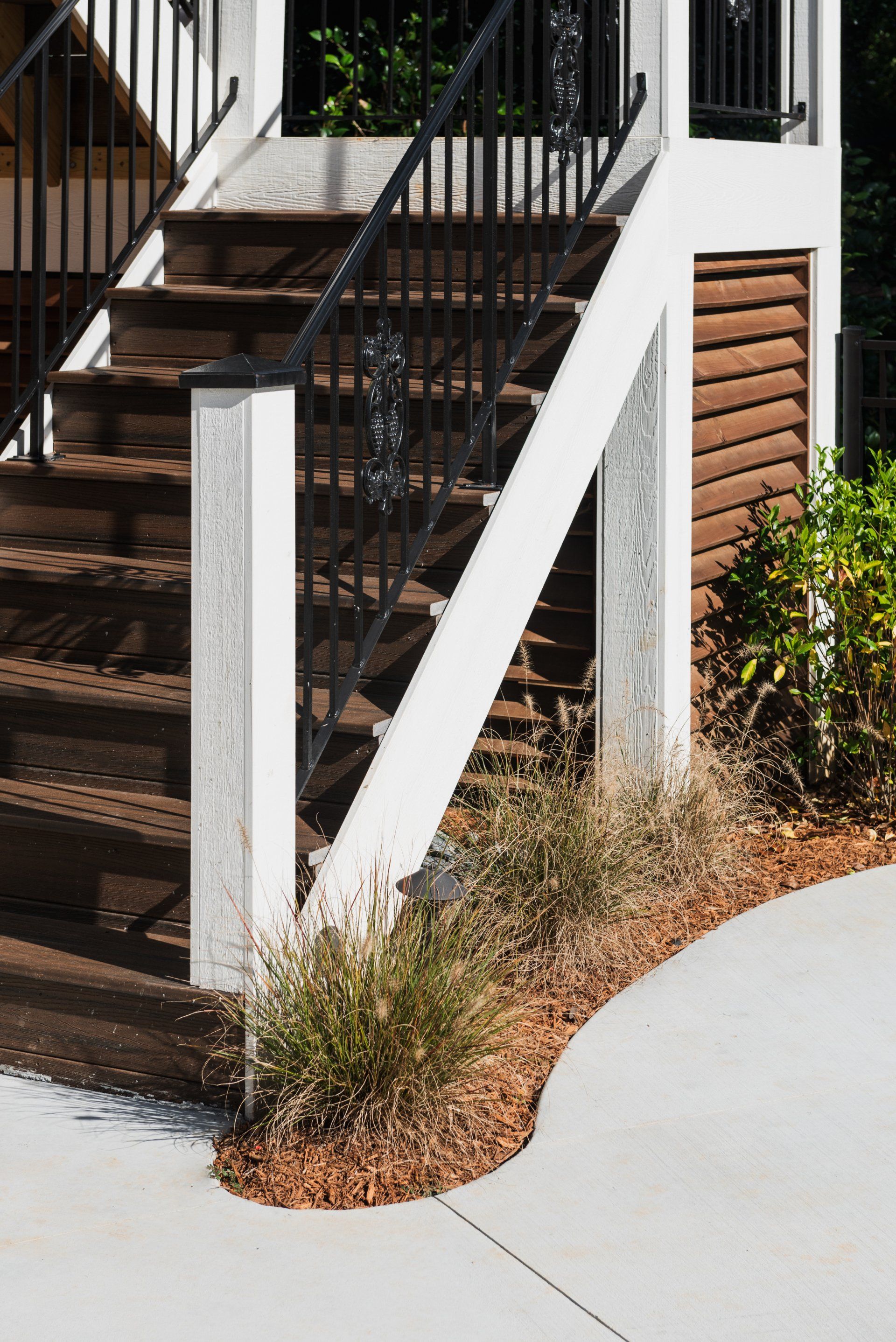 Stairway with white posts and black railing beside a sidewalk and dry landscaping
