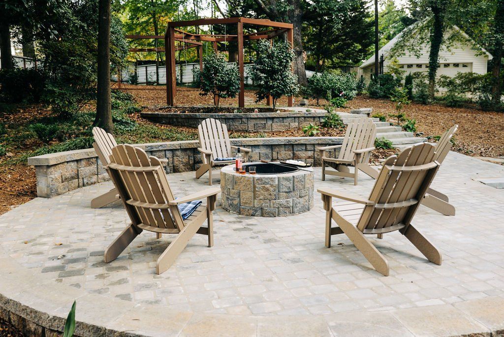 Outdoor fire pit seating area with wooden chairs around a stone circular pit in a garden patio