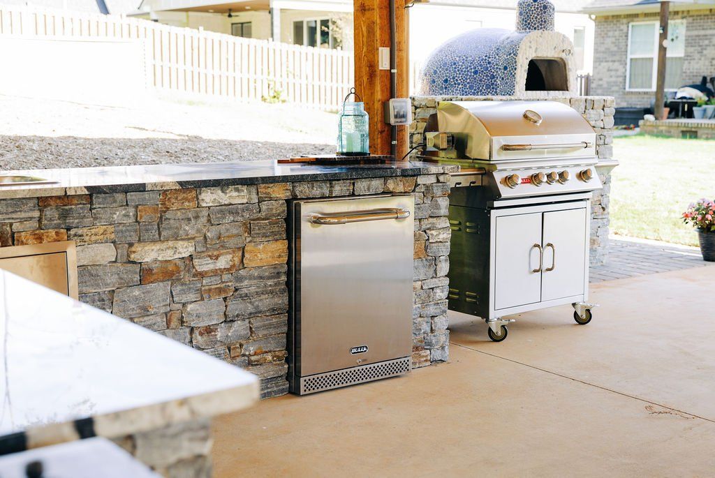 Outdoor patio with a built-in stone grill, stainless steel cabinet, and covered counter area