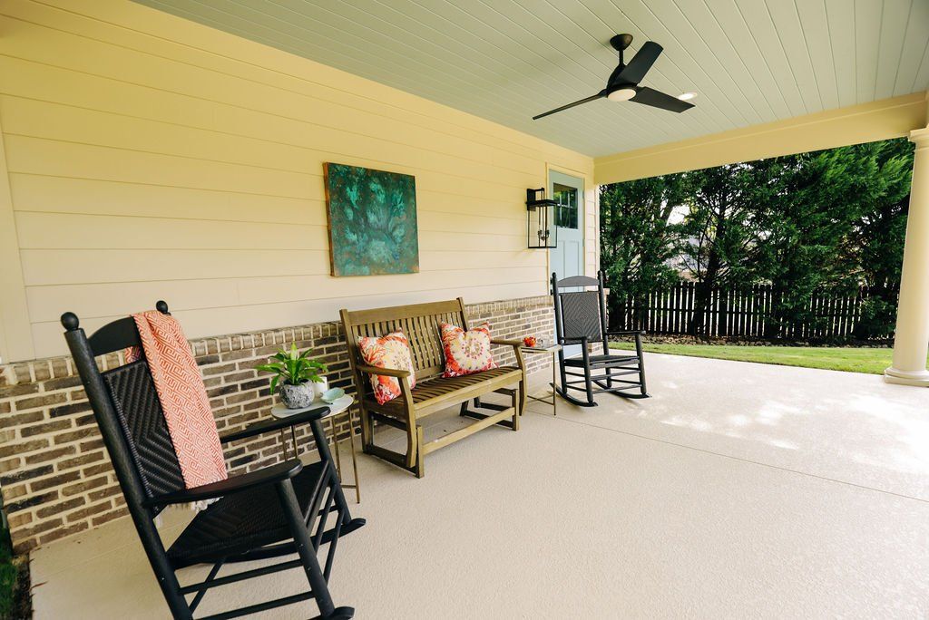 Covered porch with wicker chairs, bench, ceiling fan, and view of a green backyard through open railing.
