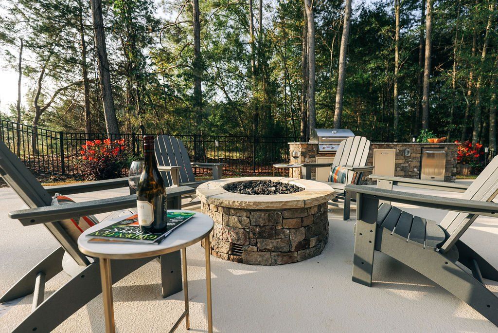 Backyard fire pit with Adirondack chairs, small table, and wooded fence line