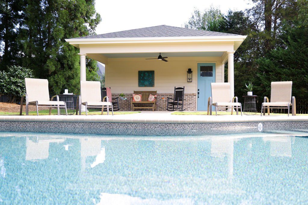 Backyard pool with lounge chairs and a patio beside a yellow house