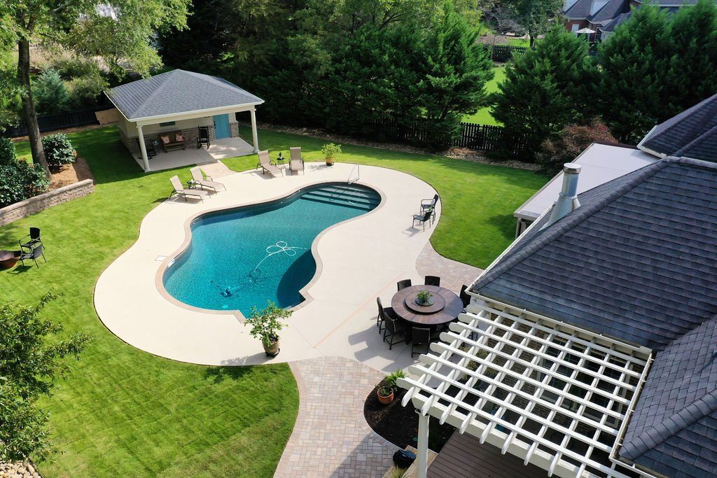 Aerial view of a backyard with a kidney-shaped swimming pool, patio, gazebo, and lush green lawn.