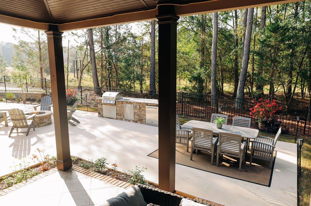 Covered patio with dining tables overlooking a wooded backyard and outdoor grill area