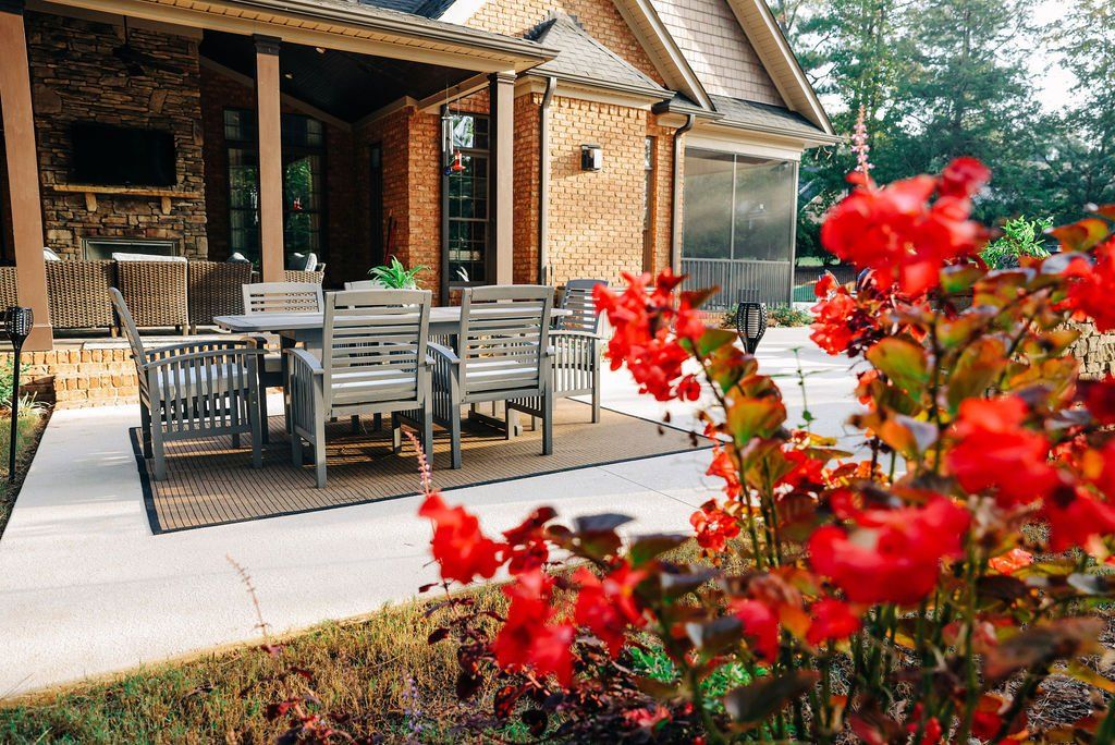 Brick patio dining area with wicker furniture and bright red flowers in the foreground