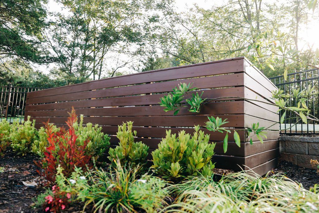 Modern brown wooden garden planter with lush green and red plants in a sunny yard
