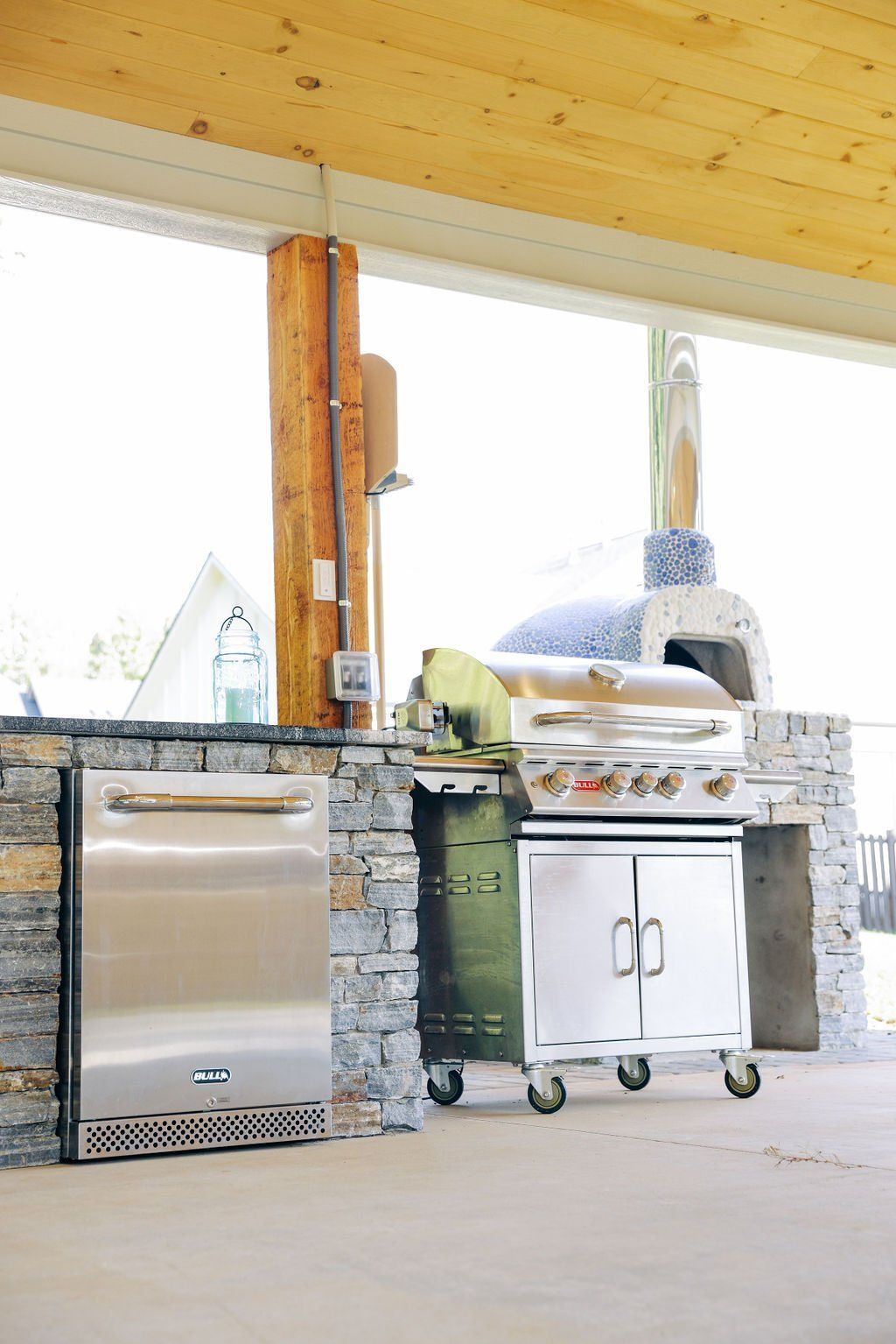 Outdoor patio with a built-in stainless grill, stone countertop, and cabinet under a covered wooden roof