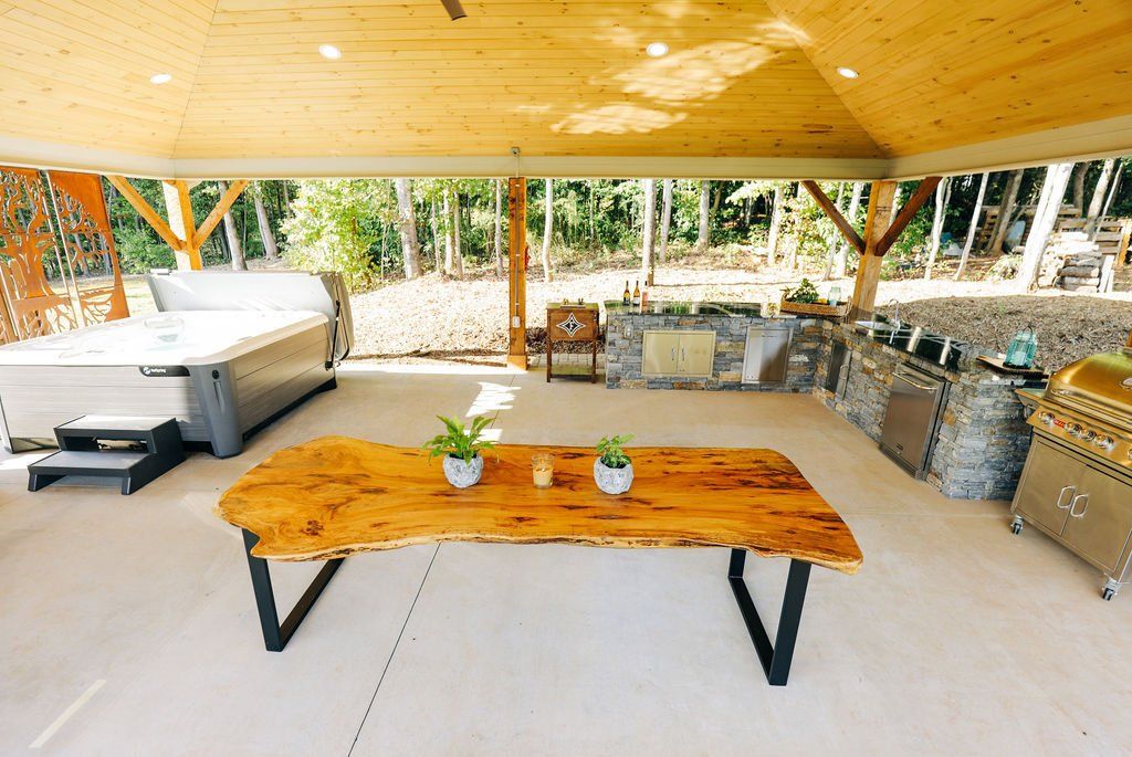 Covered patio with wooden table, sofas, and outdoor seating under a wood سقف-like roof