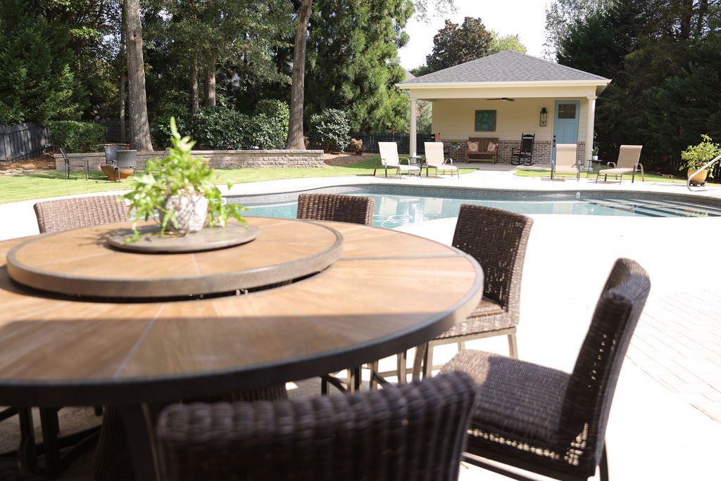 Patio table and chairs beside a swimming pool with a small building in the background