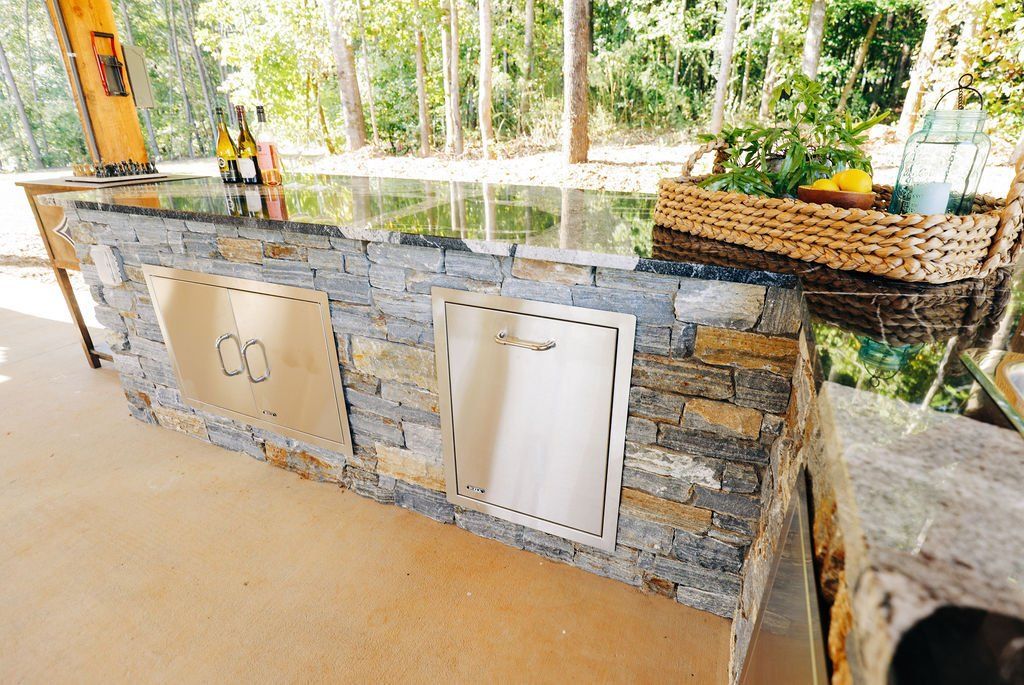 Stone outdoor grill with metal cabinet doors and a woven basket on top in a patio setting