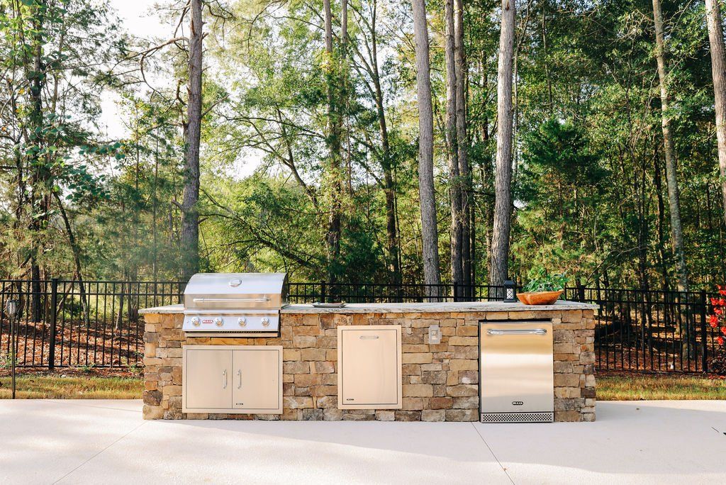 Outdoor stone barbecue grill with cabinets in a wooded backyard patio