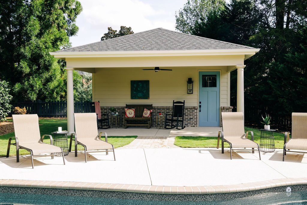 Poolside patio with lounge chairs and a covered seating area in front of a house