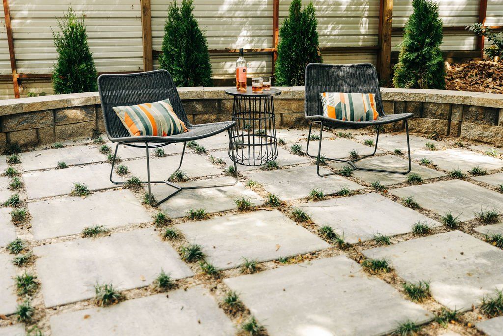 Outdoor patio with two black chairs, striped cushions, and a small table on stone pavers