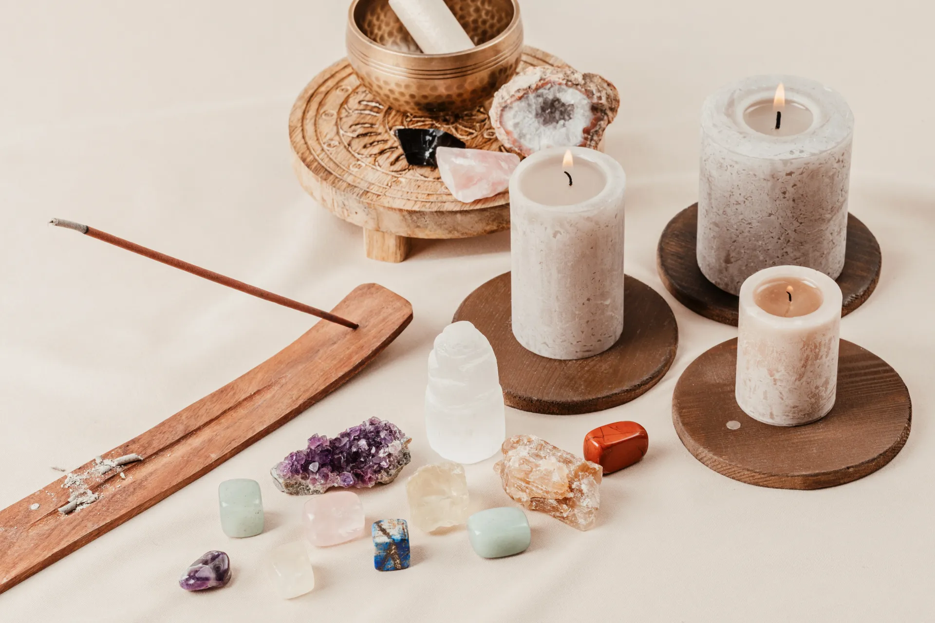 Candles, crystals, and a singing bowl on a cream-colored cloth, promoting relaxation.