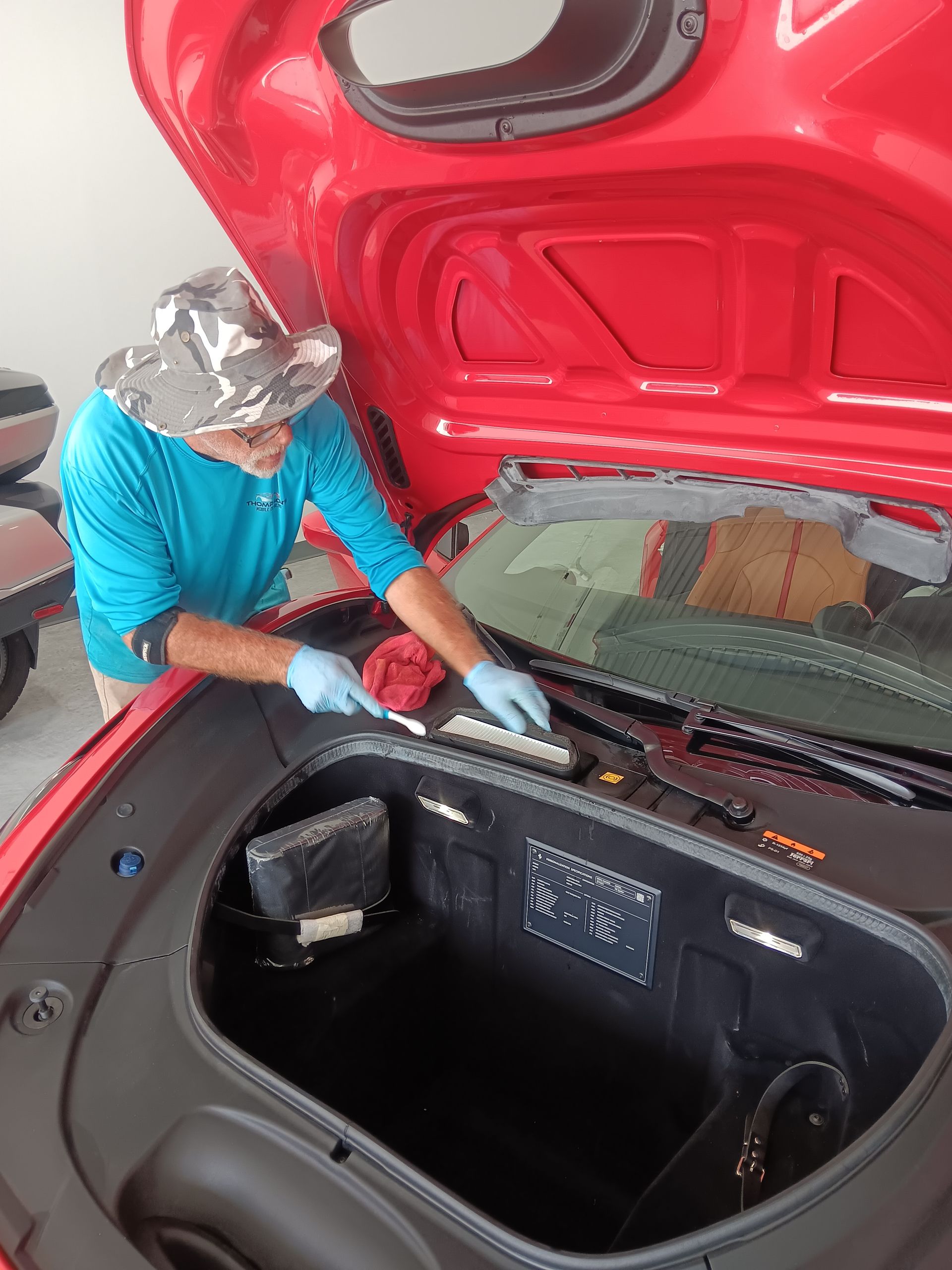 Man inspecting a yellow sports car in a garage, polishing the front hood.