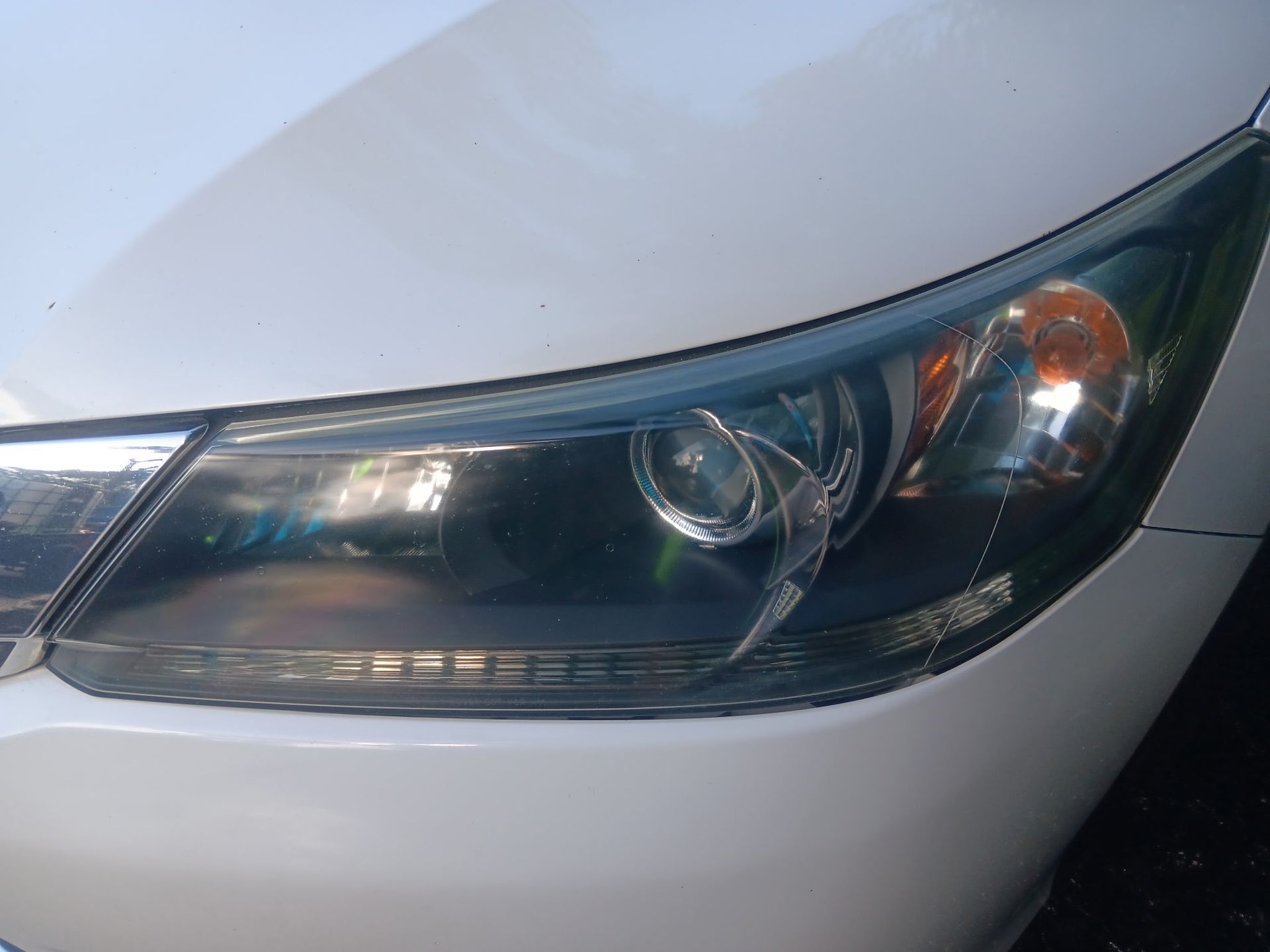 Close-up of a car's front headlight on a white vehicle, showing a sleek, dark-tinted lens.