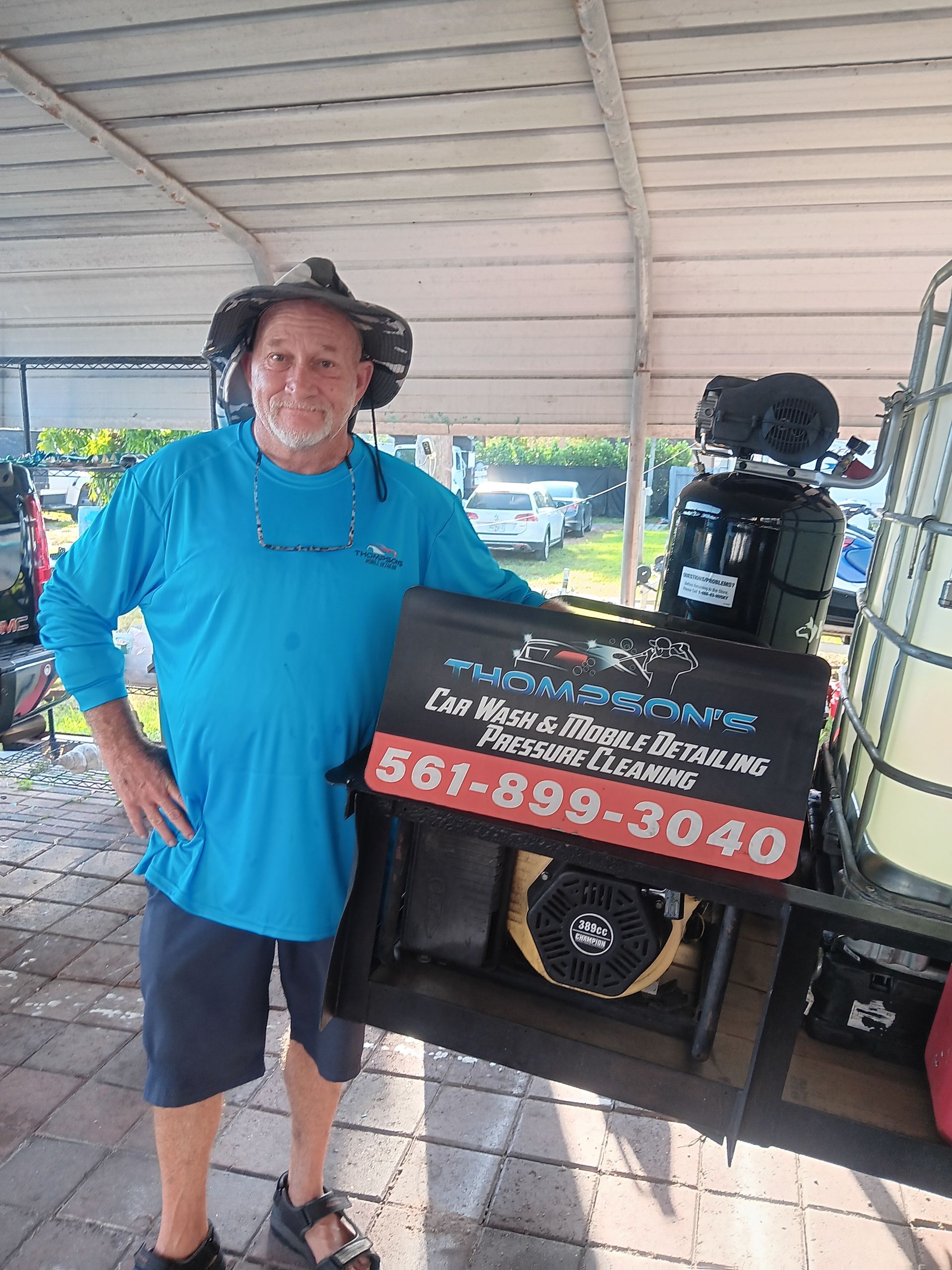 Man in blue shirt beside outdoor speaker display with sign and phone number under a covered pavilion