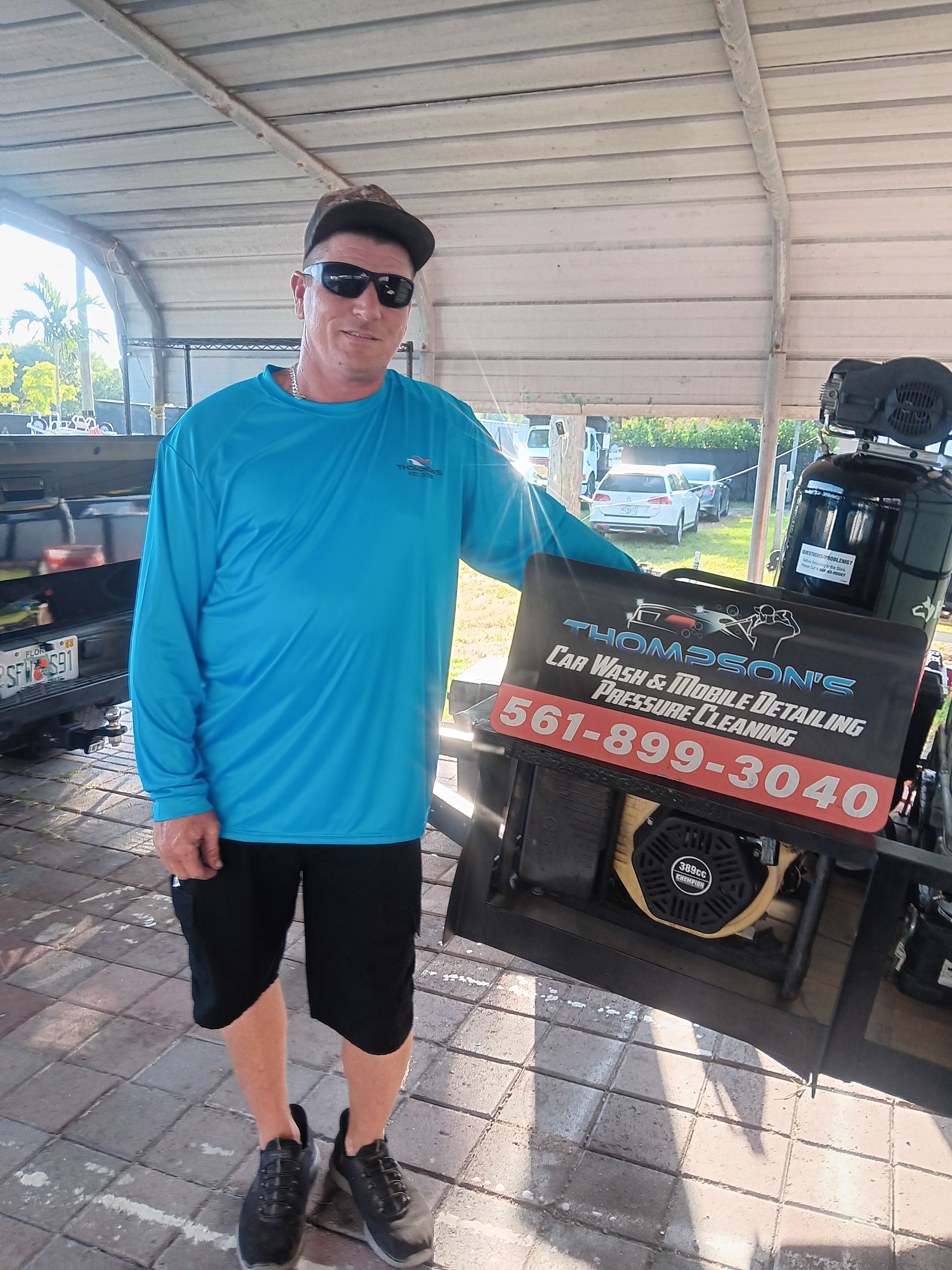 Man in blue shirt and sunglasses standing by a promotional cart under a covered outdoor area.