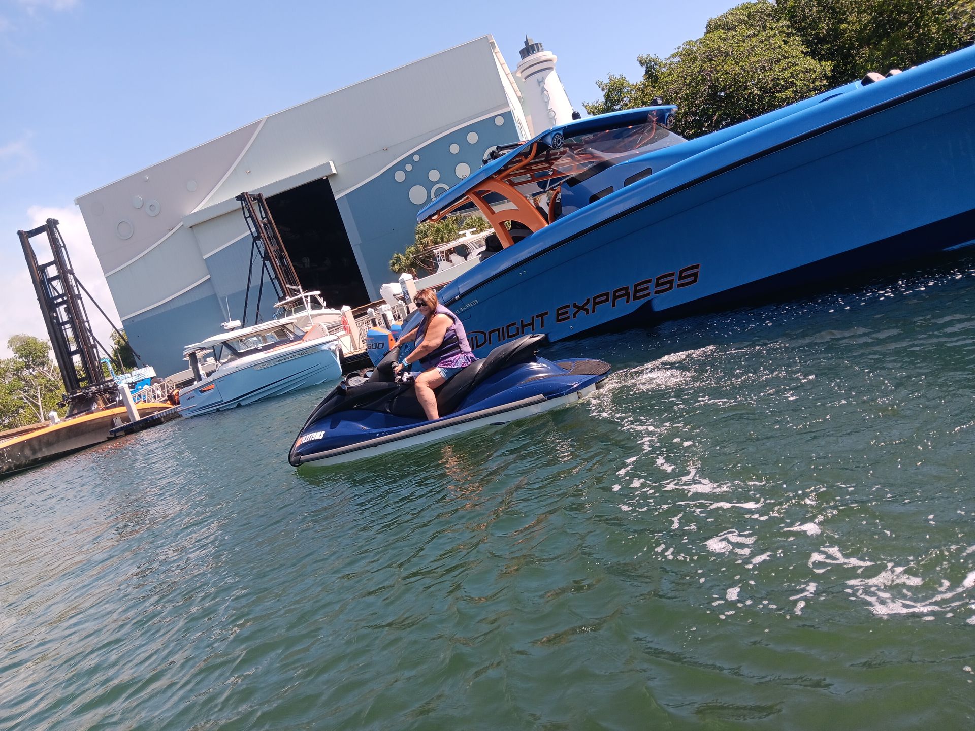 Person riding a jet ski beside a blue yacht on choppy water near a dock