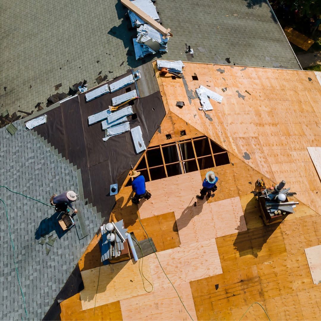 Roofers installing orange shingles on a house roof, with several workers and exposed gray underlayment.