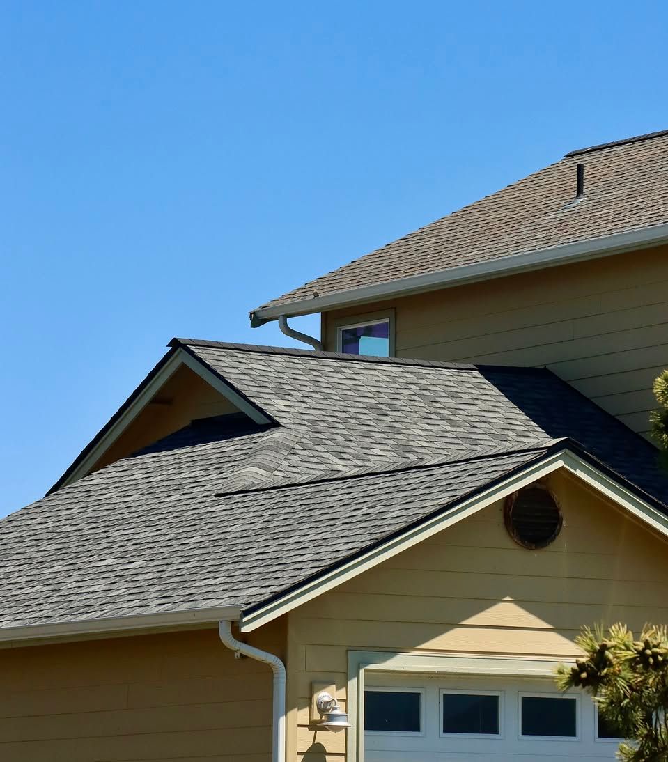 Suburban house with gray shingled roof and tan siding under a clear blue sky
