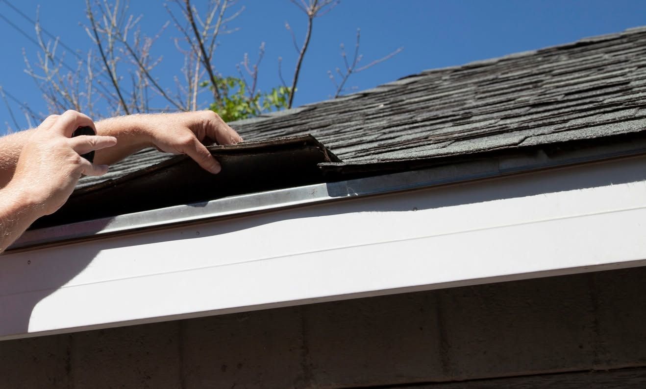 Hands lifting a shingle on a house roof above a white gutter