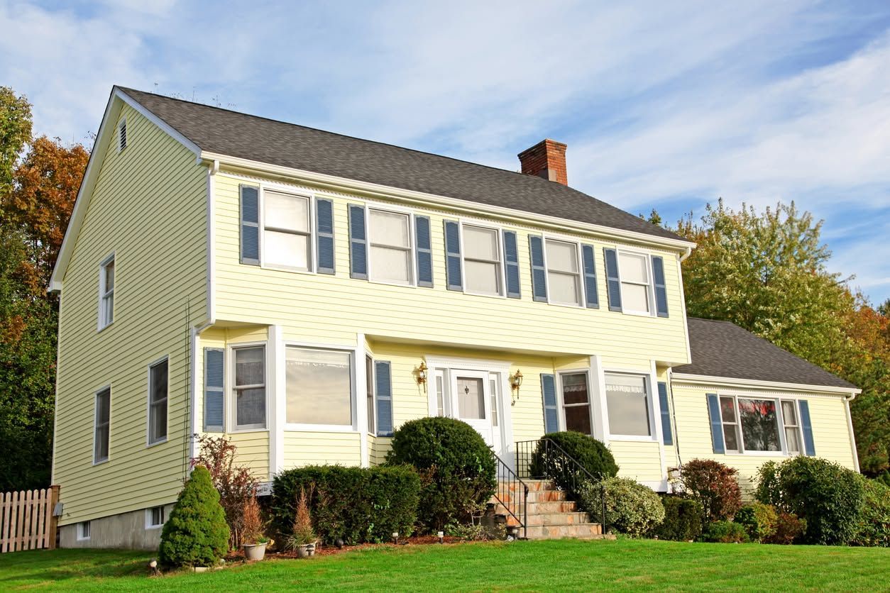 Two-story yellow house with white trim, front steps, and landscaped lawn under a blue sky