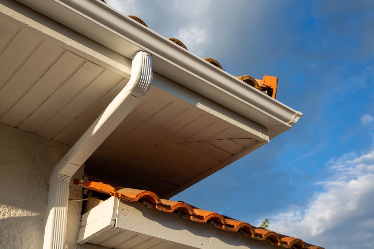 Close-up of a house roof with white gutter, terracotta tiles, and blue sky