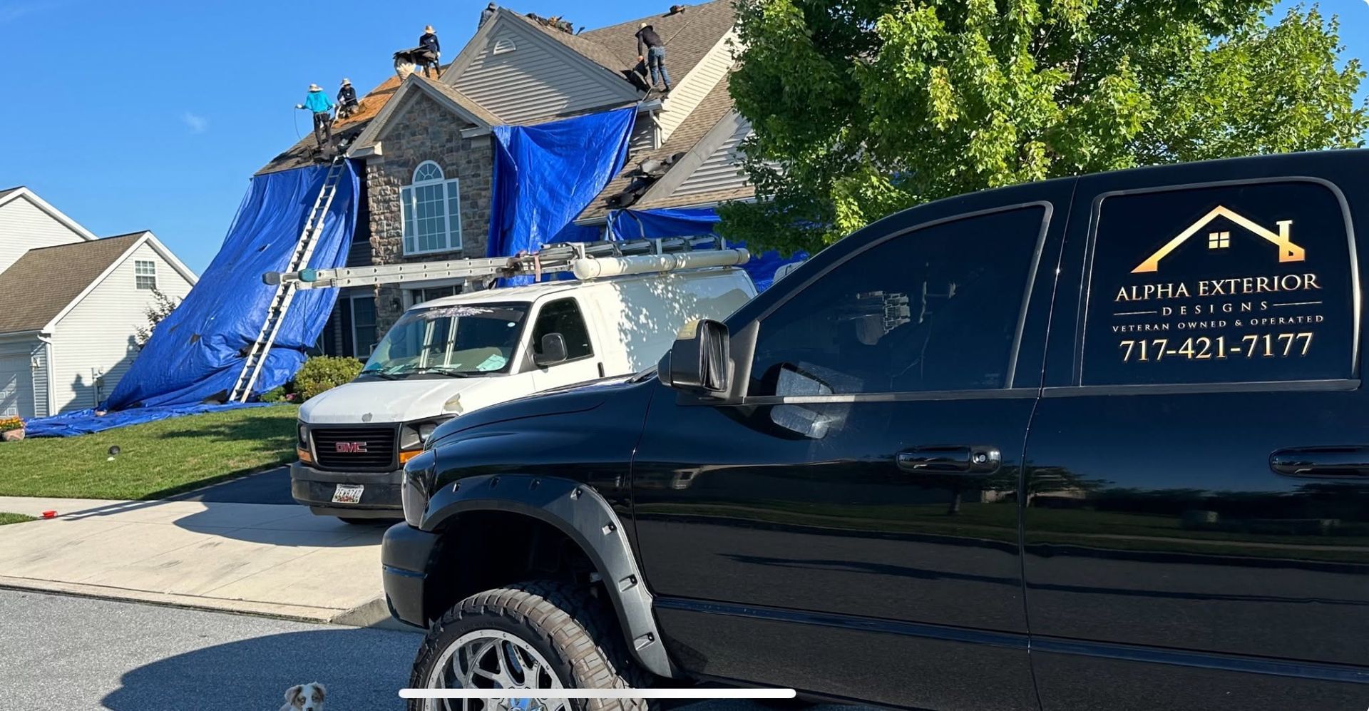 Black pickup truck parked in front of a house under construction with blue tarp covering the roof.