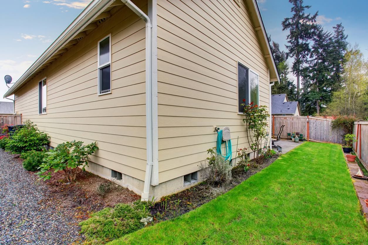 Side view of beige house with green lawn, landscaped beds, and fence along the yard