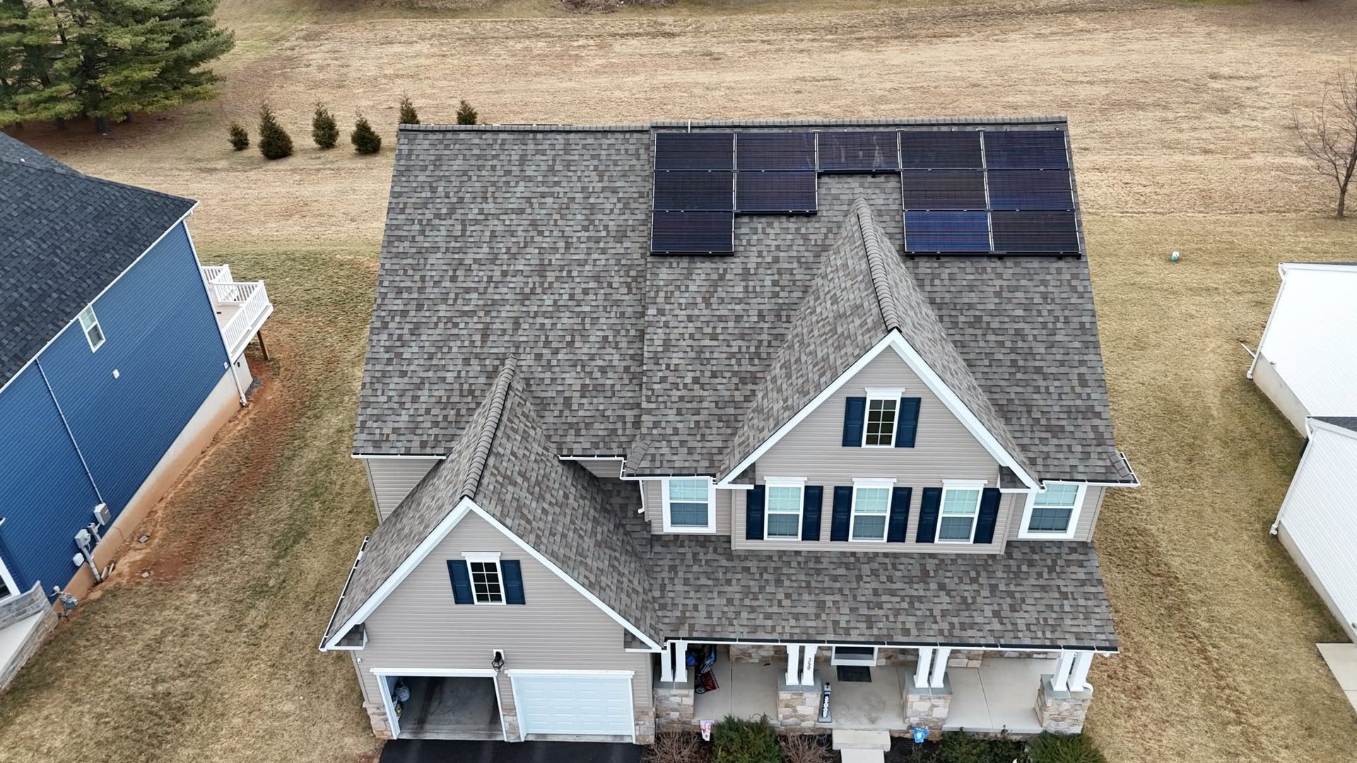 Aerial view of a gray house with black roof solar panels and a white garage in a suburban yard
